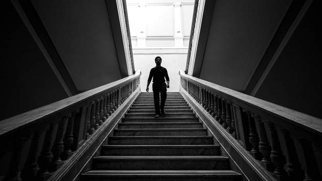 Silhouette of a man descending a grand marble staircase in a historic building