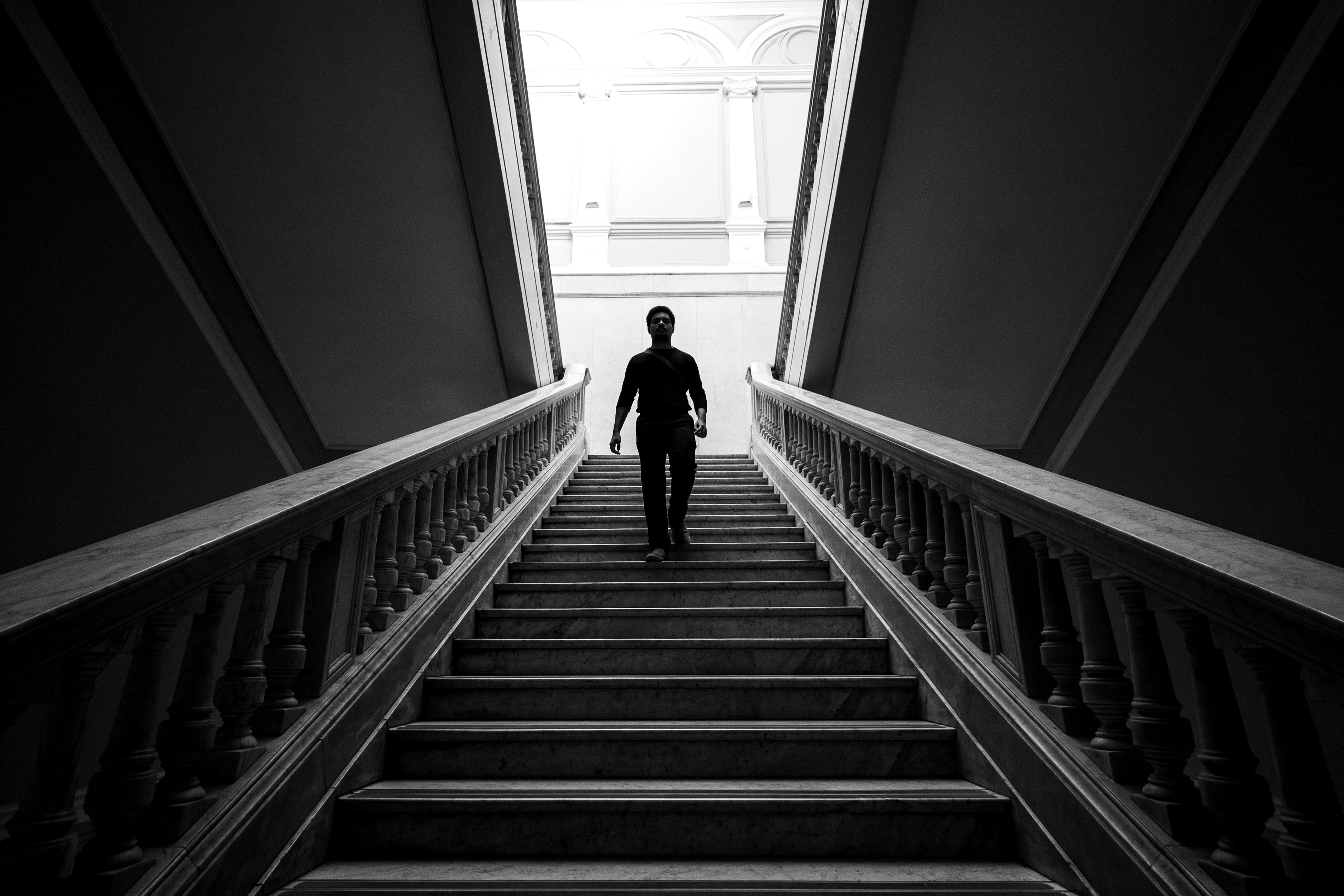Silhouette of a man descending a grand marble staircase in a historic building